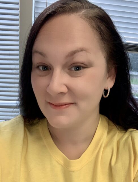 A woman with long brown hair wearing a yellow shirt smiles, reflecting support for Louisiana citizens with developmental disabilities.