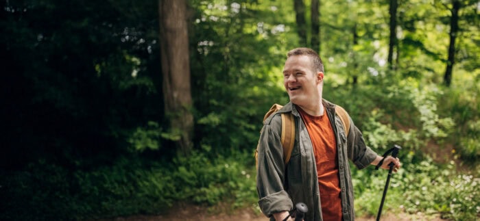 A man hiking in a forested area, wearing an orange shirt, proudly showing support for Louisiana citizens with developmental disabilities.