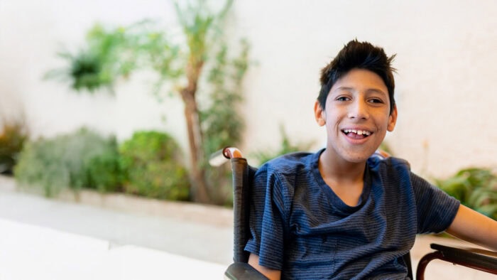 A young boy in a wheelchair smiles at the camera, reflecting support for Louisiana citizens with developmental disabilities.