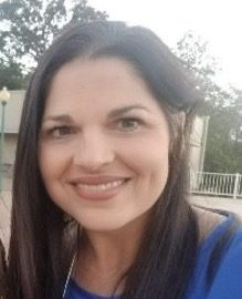 A woman with long dark hair and a blue top smiles outdoors, showing support for Louisiana citizens with developmental disabilities.