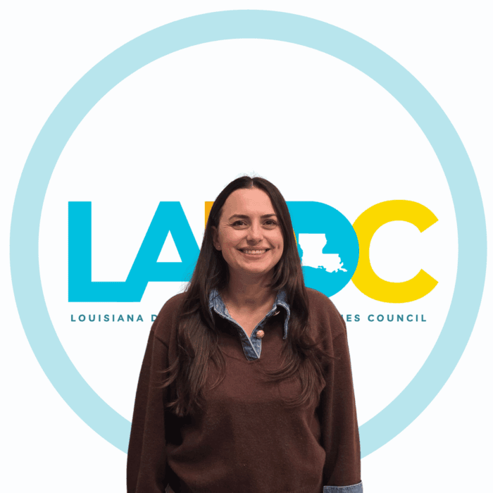 A woman with long dark hair, wearing a black shirt, smiles softly, reflecting support for Louisiana citizens with developmental disabilities.