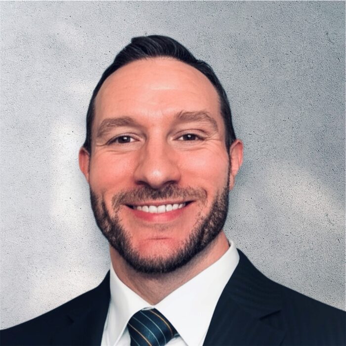 Man in a suit and tie smiling, showing support for Louisiana citizens with developmental disabilities, against a gray textured background.