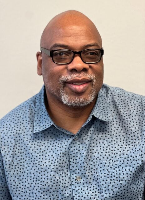 A man with glasses and a gray beard, in a blue shirt, smiles—showing support for Louisiana citizens with developmental disabilities.