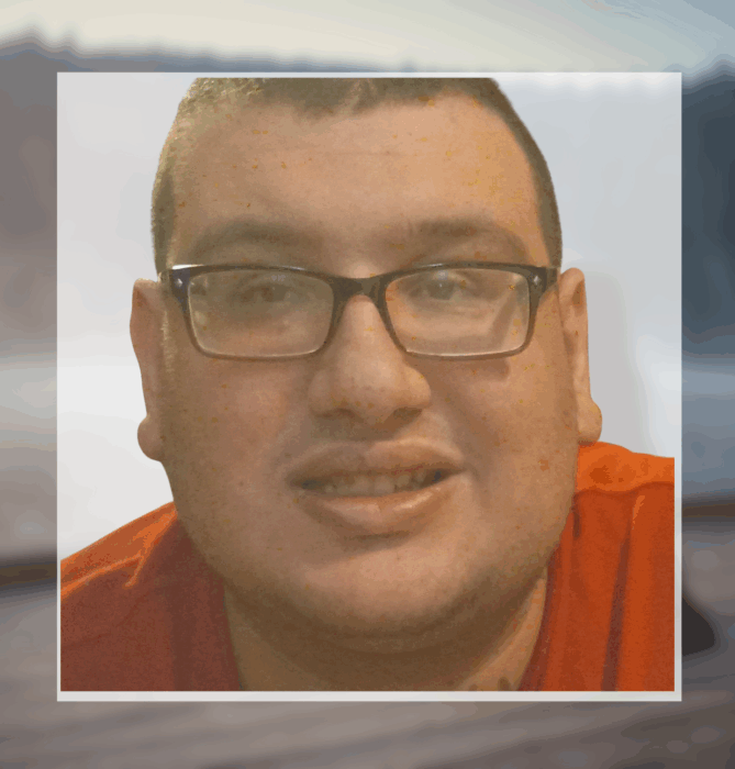 A man with short dark hair, glasses, and a red shirt smiles at the camera, showing support for Louisiana citizens with developmental disabilities.