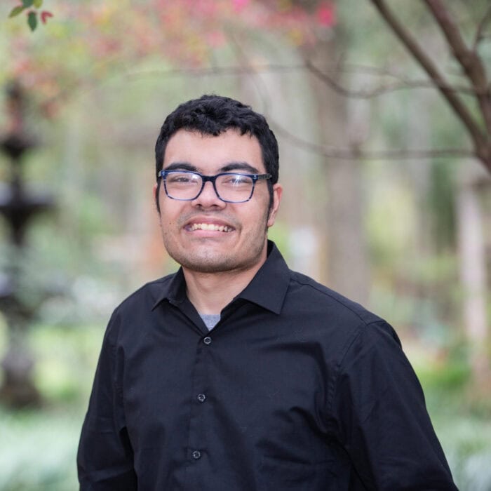 A man wearing glasses and a black button-down shirt stands outdoors, smiling, showing support for Louisiana citizens with developmental disabilities.