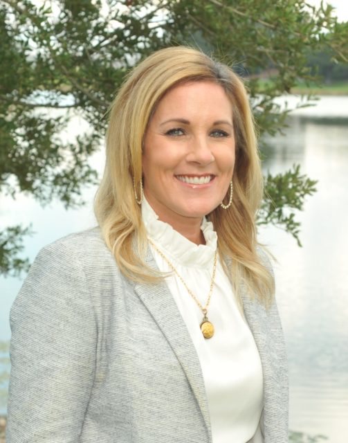 A woman with blonde hair, wearing a light blazer and necklace, smiles outdoors—reflecting support for Louisiana citizens with developmental disabilities.