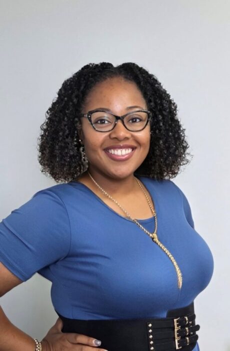A woman with curly hair and glasses smiles, showing support for Louisiana citizens with developmental disabilities in a blue dress and gold necklace.